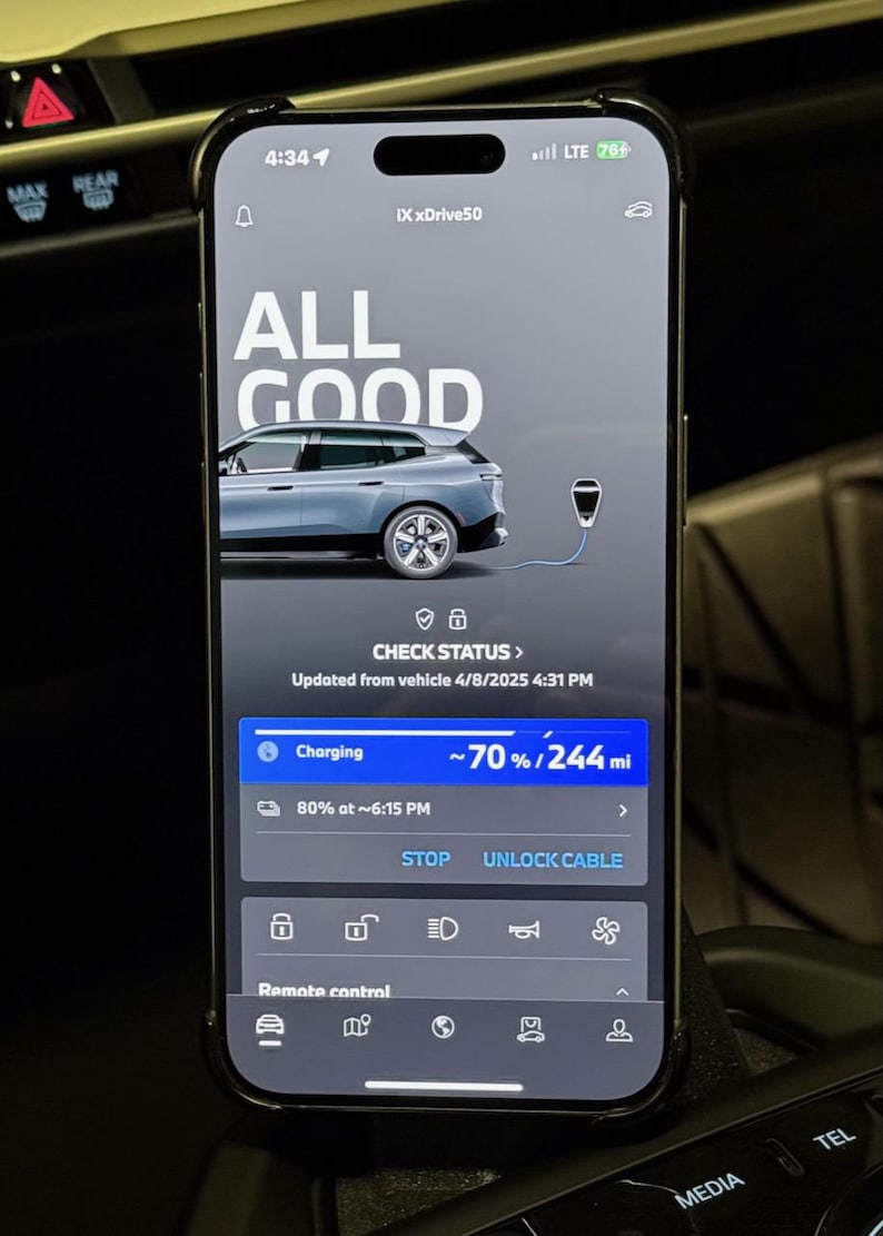 May include: A smartphone screen displaying a car charging status. The screen shows "ALL GOOD" with a picture of a car charging. The car is a silver BMW iX xDrive50. The screen shows the car is charging at 70% and has 244 miles of range. The screen also shows the time the car will be fully charged, 6:15 PM. The screen has buttons for "STOP" and "UNLOCK CABLE".