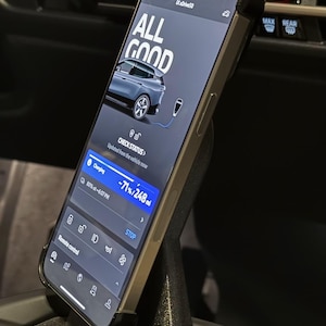 May include: A smartphone displaying a car charging app with the text "ALL GOOD" and a progress bar showing 71% charged. The app also shows the remaining range of 248 miles. The phone is mounted in a car's center console.
