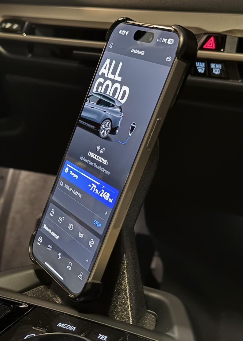 May include: A smartphone displaying a car charging app with the text "ALL GOOD" and a progress bar showing 71% charged. The app also shows the remaining range of 248 miles. The phone is mounted in a car's center console.