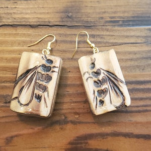 May include: A pair of wooden earrings with a gold-tone finish. Each earring features a rectangular shape with a carved design of a bee.