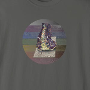 May include: A dark gray t-shirt featuring a circular graphic. The graphic depicts a colorful, abstract image of a figure on a patterned surface. The shirt has a crew neck and short sleeves. The brand name "HAUNTED IVORY" is printed on the bottom right.