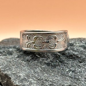 May include: A silver ring with an intricate floral design. The ring is made from recycled materials and is a unique and stylish piece of jewelry.