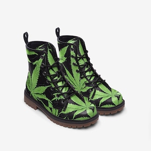 Puede incluir: Botas de cuero negro con estampado de hojas de marihuana verdes. Las botas tienen cordones y una suela marrón.