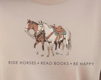 Peut inclure: Sweat-shirt beige avec un motif de deux chevaux sellés. Le texte "RIDE HORSES * READ BOOKS * BE HAPPY" est imprimé en dessous. Le sweat-shirt est de couleur neutre et a un col rond.
