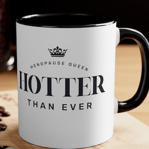 May include: White ceramic mug with a black rim and handle. The mug has a black crown graphic and the text "Menopause Queen Hotter Than Ever".