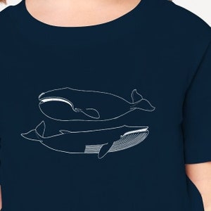 May include: Navy blue t-shirt featuring two white line-art whale illustrations. The whales are depicted in a minimalist style, with one above the other. The shirt has a round neckline and short sleeves.