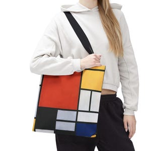 May include: Tote bag featuring a Mondrian-style geometric design with red, yellow, black, white, and blue blocks. The bag has a black strap and is carried over the shoulder. The bag is made of a durable material.