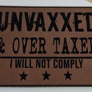 May include: Brown leather doormat with the text "UNVAXXED & OVER TAXED I WILL NOT COMPLY" in black lettering. Three black stars are at the bottom of the mat.