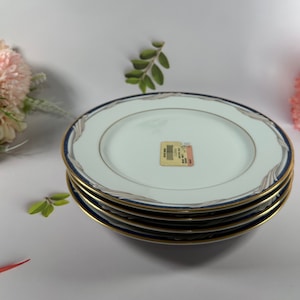 May include: Set of four white ceramic plates with a blue and gold rim. The plates have a delicate pattern on the surface.