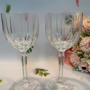 May include: Two clear glass wine glasses with a fluted design. The glasses have a tall stem and a round base.