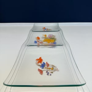 May include: A clear glass serving tray with three connected sections. The tray is decorated with colorful floral designs in orange, blue, and yellow. The tray has a rectangular shape with slightly curved edges.