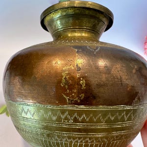 May include: A vintage brass water pot with intricate engraved designs. The pot has a rounded body and a lid with a small knob. The brass has a warm, golden color with some patina.