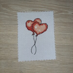 May include: Two red heart-shaped balloons tied together with black string.