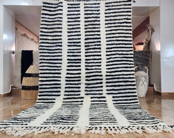 May include: A black and white striped Moroccan rug with fringe. The rug is made of wool and has a traditional design.