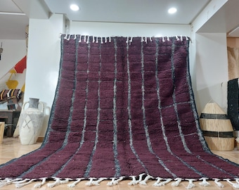 May include: A large, handwoven Moroccan rug with a striped pattern in shades of burgundy and black. The rug has a fringe border and is made of wool.