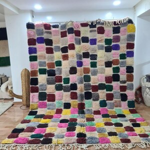 May include: A colourful Moroccan rug with a checkered pattern in shades of pink, green, yellow, red, blue, and grey. The rug has a fringe border and is made of wool.