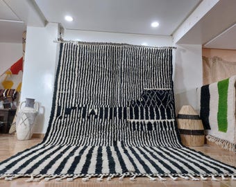 May include: Black and white striped rug with a geometric pattern in the center. The rug is made of wool and has a fringe border.