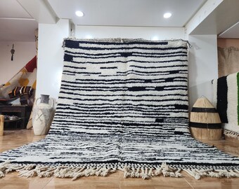 May include: A large, rectangular rug with a white background and bold black horizontal stripes. The rug has a fringe along the bottom edge. The design is simple and modern, suitable for various interior styles.