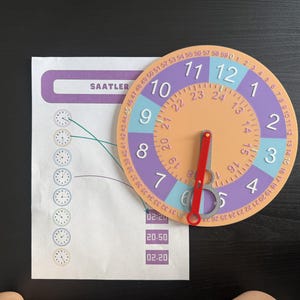 May include: A circular educational clock tool with a peach centre, purple and blue outer rings featuring numbers 1 through 12, and a minute track from 0 to 59. A red hand points to the 6. Beside it is a worksheet with the text SAATLER and clock icons.