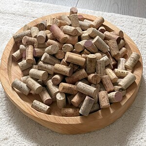 Pode incluir: Uma tigela de madeira cheia de uma coleção de rolhas de vinho usadas. As rolhas são de vários tons de marrom e bege, algumas com texto impresso e etiquetas.