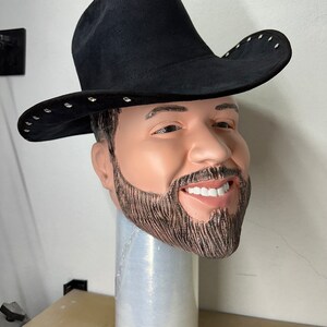 May include: A black cowboy hat with silver studs around the brim. The hat is worn on a mannequin head with a beard.