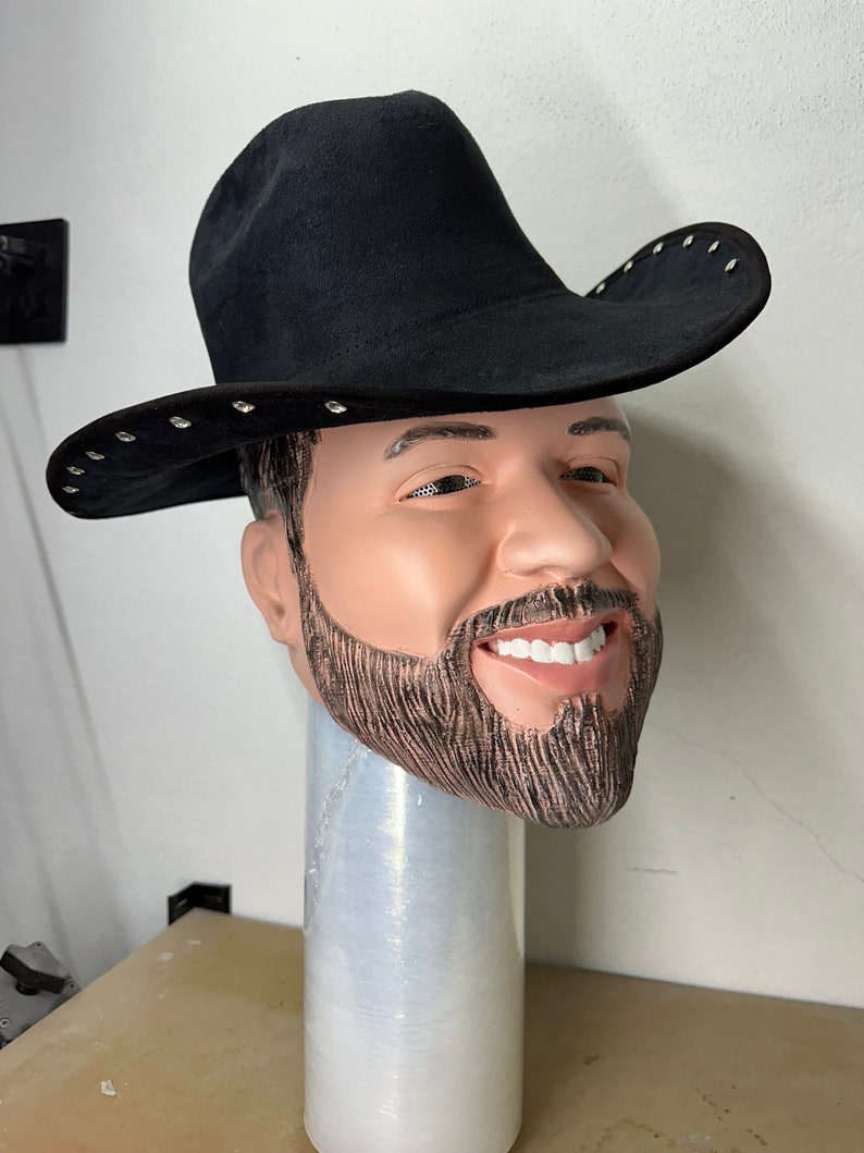 May include: A black cowboy hat with silver studs around the brim. The hat is worn on a mannequin head with a beard.
