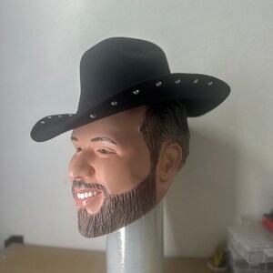May include: A black cowboy hat with silver studs. The hat is being worn by a person with a beard and moustache. The hat is on a white stand.