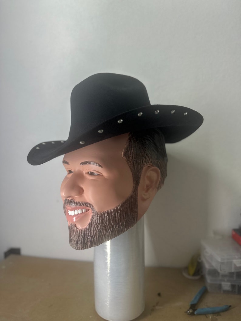 May include: A black cowboy hat with silver studs. The hat is being worn by a person with a beard and moustache. The hat is on a white stand.