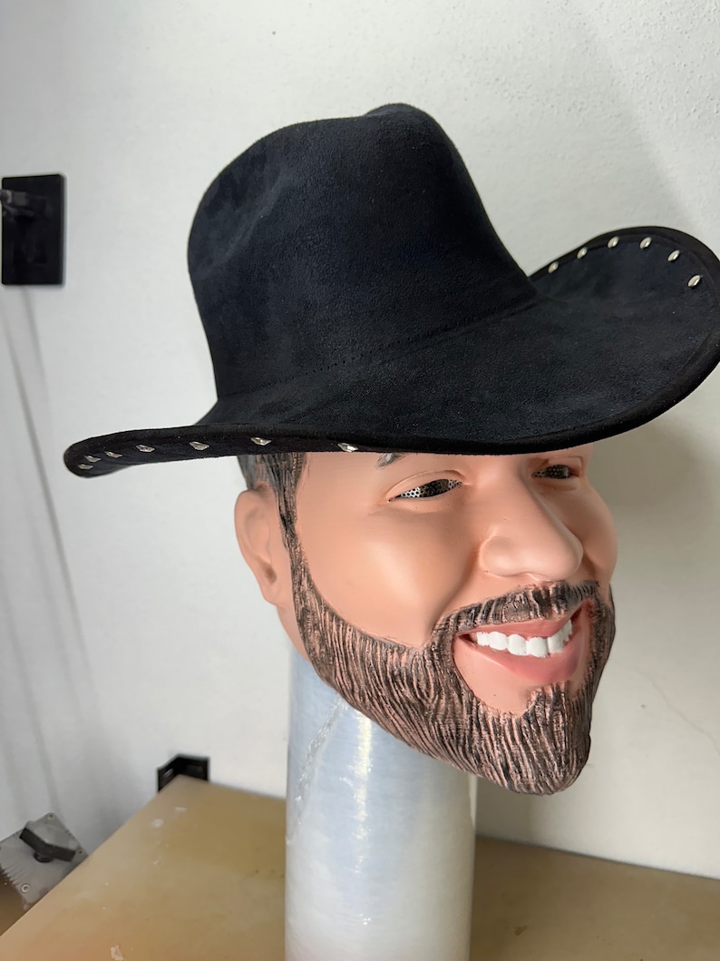 May include: A black cowboy hat with silver studs around the brim. The hat is made of suede and has a wide brim. The hat is sitting on a mannequin head with a beard.