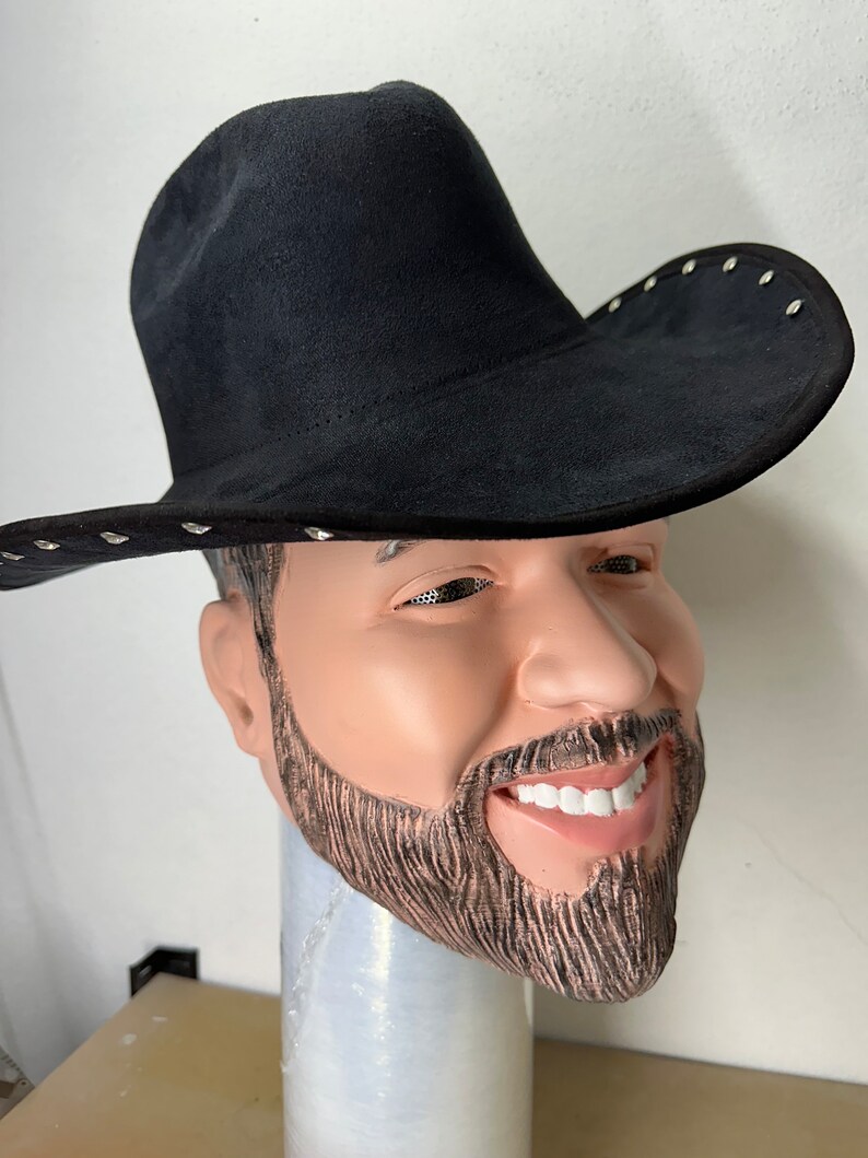 May include: A black cowboy hat with silver studs around the brim. The hat is being worn by a person with a beard and moustache.