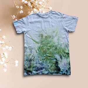 May include: A light blue t-shirt with a tie-dye pattern in shades of green, blue, and purple. The dye is concentrated at the bottom of the shirt, creating a gradient effect.