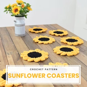 May include: Crochet pattern for sunflower coasters. Six yellow crocheted coasters with black centers are arranged on a wooden table.