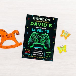 May include: A black and green birthday party invitation with a neon green video game controller graphic. The invitation reads "Game On! Calling all gamers! David's has reached Level 10". The invitation also includes the date, time, and location of the party.