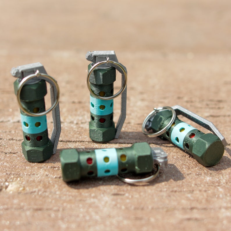 May include: Four green and blue grenade keychains with silver rings. The keychains are made of plastic and have a realistic design.