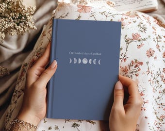 May include: A blue hardcover journal with the text "One hundred days of gratitude" and a row of moon phases printed in white.