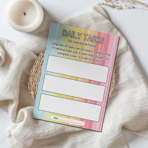 May include: A printable daily task list with a rainbow watercolour background. The text reads "DAILY TASKS for overactive minds. Long lists of tasks can be totally overwhelming. Try writing down just 3 tasks that you want to complete today, in order of priority. Date."