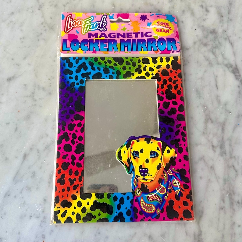 Puede incluir: Un espejo magn&eacute;tico para taquilla Lisa Frank en un paquete colorido. El marco tiene un dise&ntilde;o de estampado de leopardo arco&iacute;ris. Un perro d&aacute;lmata de dibujos animados est&aacute; en la parte inferior derecha. El texto "Lisa Frank MAGNETIC LOCKER MIRROR" est&aacute; en la parte superior.