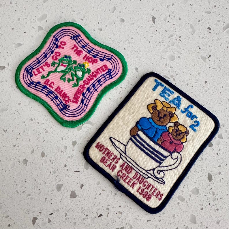 Puede incluir: Dos parches bordados. Uno es rosa con ribete verde, con ranas y notas musicales, con el texto "Let's Go to the Hop Father-Daughter B.C. Dance". El otro es color crema con borde azul marino, que representa osos en una taza de t&eacute;, con el texto "Tea for 2" y "Mothers and Daughters Bear Creek 1988."