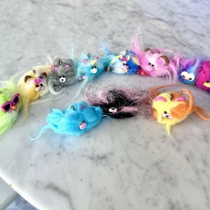 May include: A collection of colorful, handmade felted animal toys. Each toy features a unique design with different colors, including pink, blue, yellow, and purple. Some have sunglasses or horns. These whimsical creatures are perfect for children's play or as decorative items.