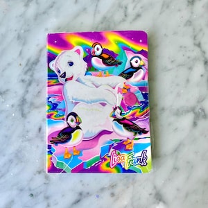 May include: A notebook with a colourful design featuring a polar bear and puffins. The cover has a rainbow background with pink, purple, blue, and green hues. The Lisa Frank logo is visible in the bottom right corner. The notebook is a vibrant stationery item.