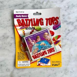May include: A vintage Battling Tops keychain on a yellow and white card. The card features the text "Battling Tops" in red, with a graphic of children playing with spinning tops. The keychain is for ages 6 and up.