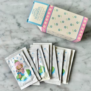 May include: A pink and blue box with the text "Avon Little Blossom Bubble Bath Packets" and a floral pattern. The box contains ten individual packets of bubble bath, each with a cartoon image of a girl in a flower dress.