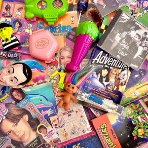 May include: A collection of vintage toys, magazines, and comics. The toys include a green spaceship, a pink Polly Pocket, a purple microphone, and a troll doll. The magazines include Disney Adventures, and a magazine called "Fangin' Tough". The comics include a Teenage Mutant Ninja Turtles comic.