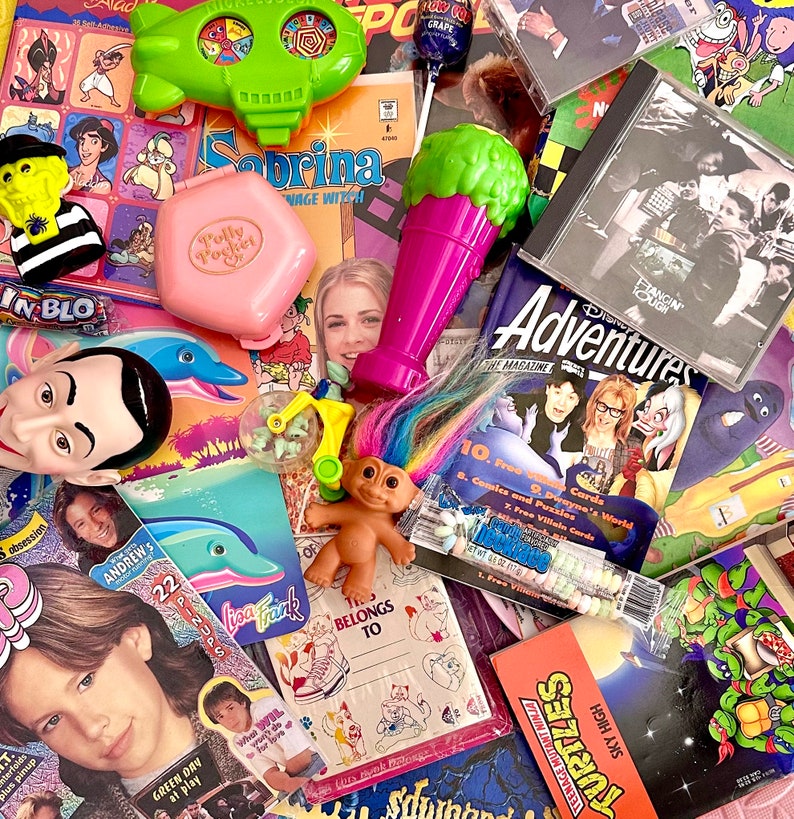 May include: A collection of vintage toys, magazines, and comics. The toys include a green spaceship, a pink Polly Pocket, a purple microphone, and a troll doll. The magazines include Disney Adventures, and a magazine called "Fangin' Tough". The comics include a Teenage Mutant Ninja Turtles comic.