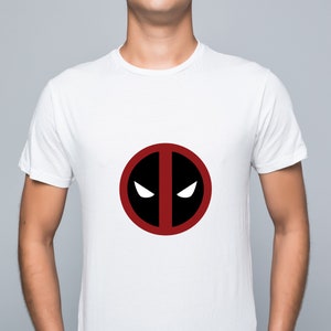 Puede incluir: Camiseta blanca con un logotipo de Deadpool rojo y negro.