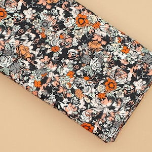 May include: Black fabric with a floral print featuring orange, white and pink flowers. The fabric is folded in half and the background is a light brown.