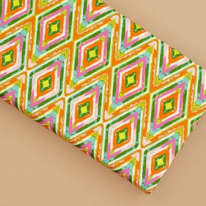 Puede incluir: Una tela blanca con un patrón geométrico colorido. El patrón presenta diamantes naranjas, verdes, rosas y amarillos.