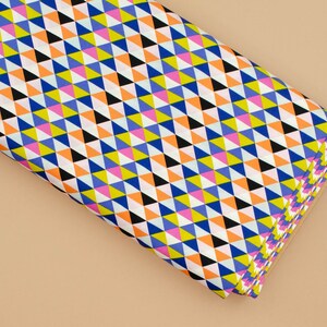 May include: A folded piece of fabric with a geometric pattern of colorful triangles in shades of blue, orange, yellow, pink, and black on a white background.