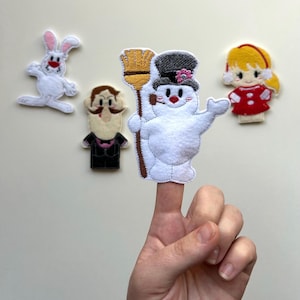May include: A collection of felt finger puppets featuring a snowman with a broom, a girl in a red dress, a rabbit, and a man with a mustache. The snowman is on a finger.