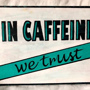 May include: A white wooden sign with black and teal lettering that reads "In Caffeine We Trust".